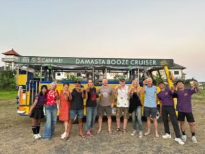 A large group of guests and team members posing beside the yellow Damasta Booze Cruiser.