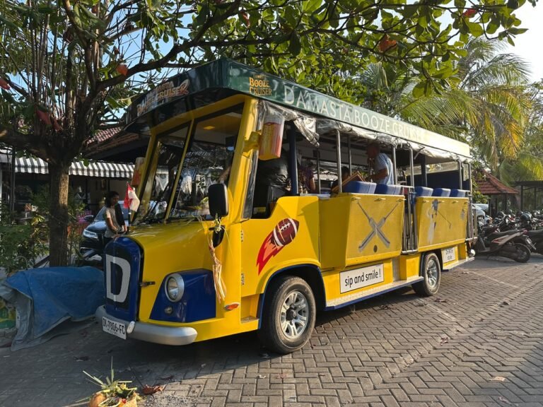 Yellow and blue Damasta Booze Cruiser parked beneath trees, viewed from the front left.