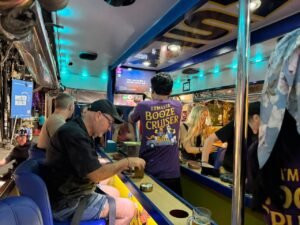 Guests at the onboard bar beneath turquoise ceiling lights inside Damasta Booze Cruiser.