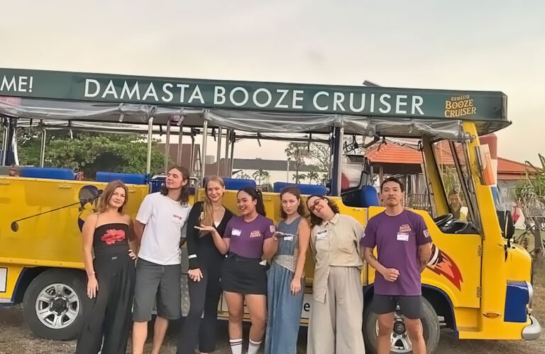 Guests and purple-shirted Damasta team members posing together beside the yellow beer bus.