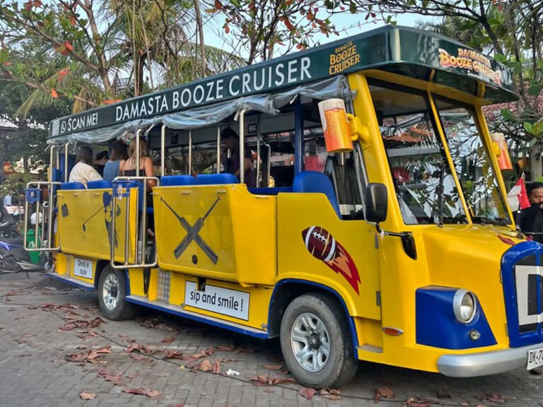 Front-right view of the yellow and blue Damasta Booze Cruiser parked beneath leafy trees.