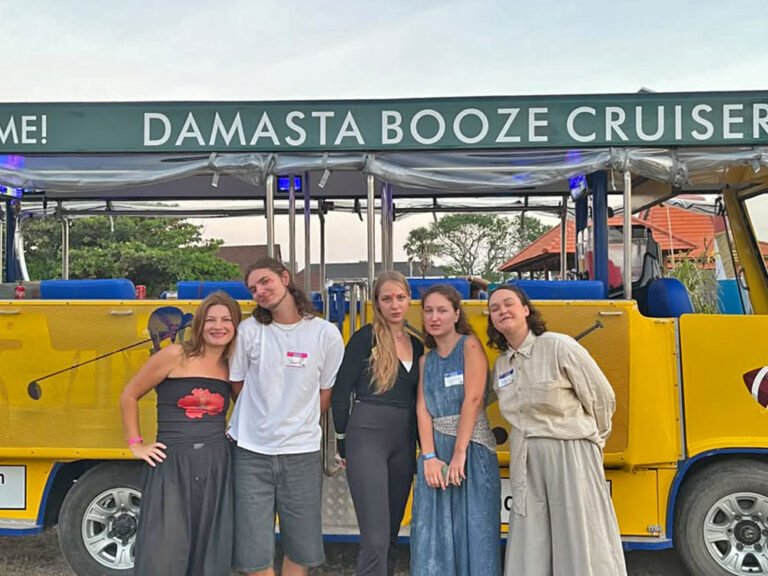 Five guests standing together beside the yellow Damasta Booze Cruiser beneath its branded roof.