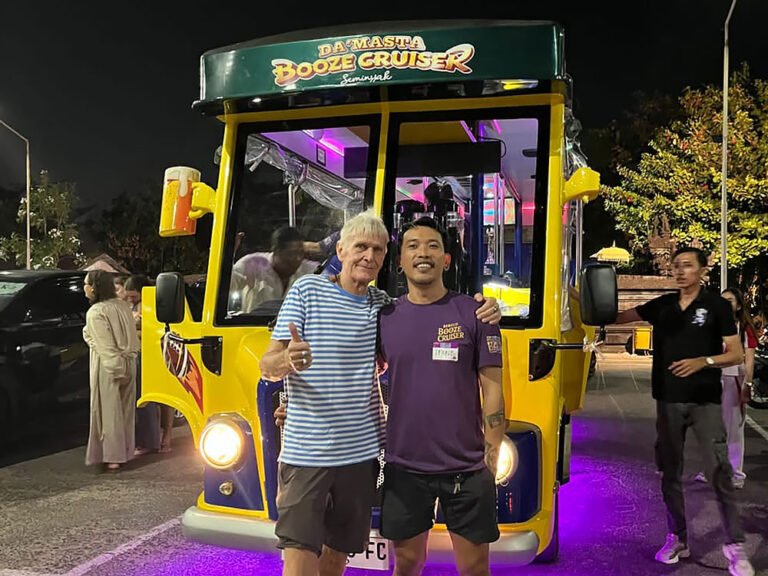 Two guests posing in front of Damasta Booze Cruiser at night with headlights and purple lighting.